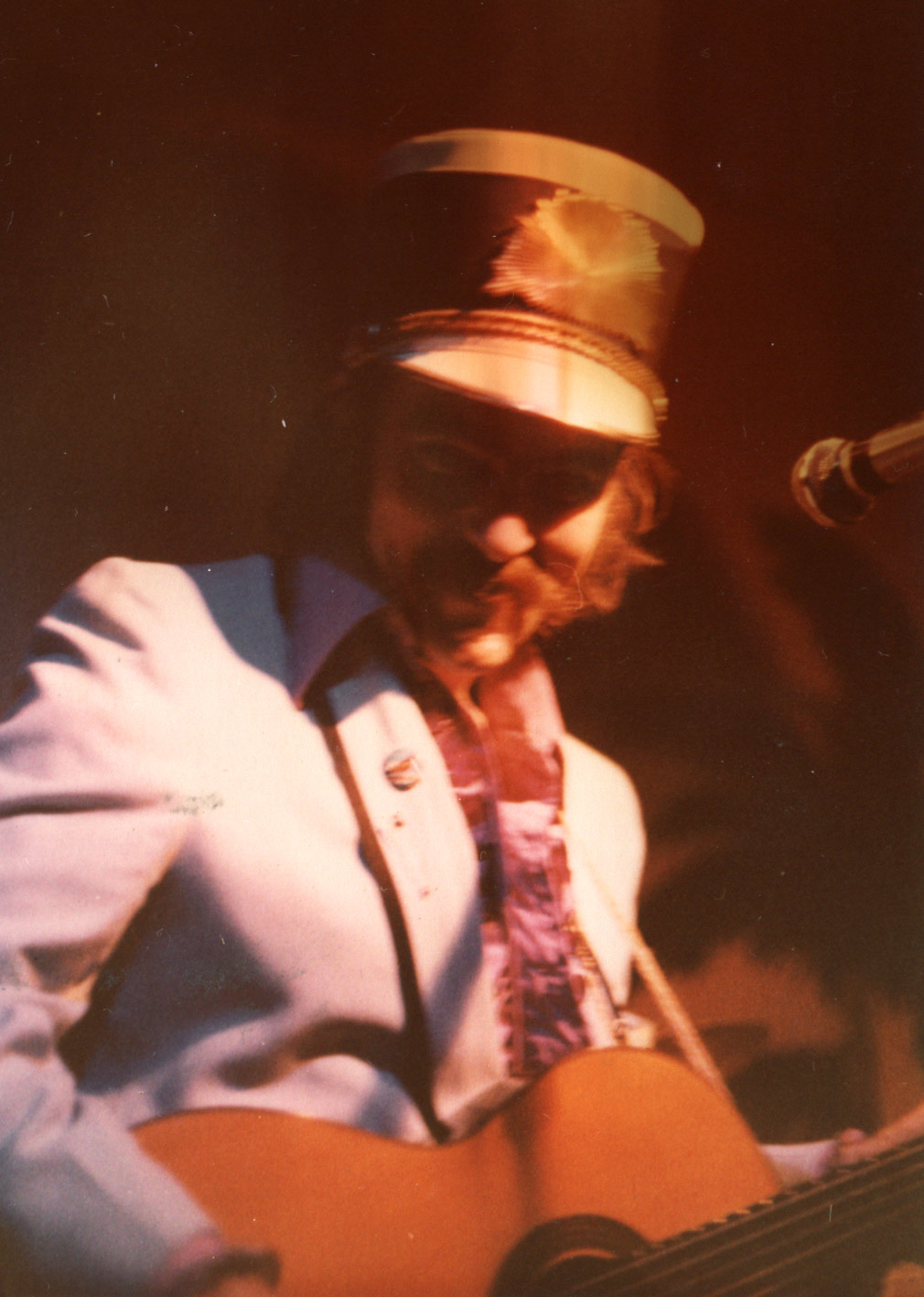 Blaze wearing tall marching band helmt, playing guitar smiling to camera