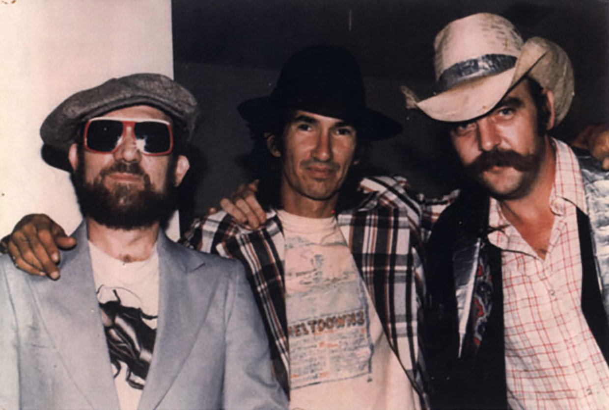 Group photo of Rex Bell in sunglasses, Townes Van Zandt in black Fedora and Blaze Foley with ductxedo and duct tape cowboy hat